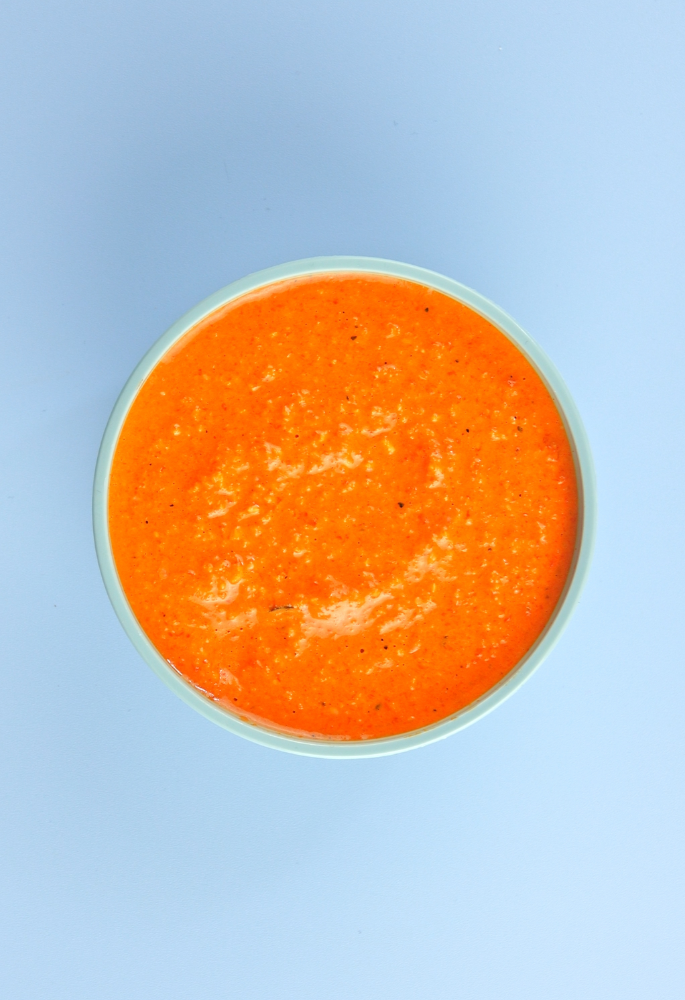 Pot of romesco sauce on a blue background