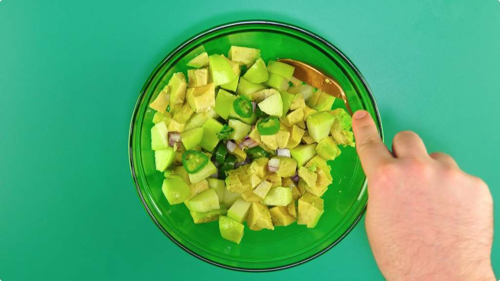 Mixig apple and avocado with a dressing in a glass bowl