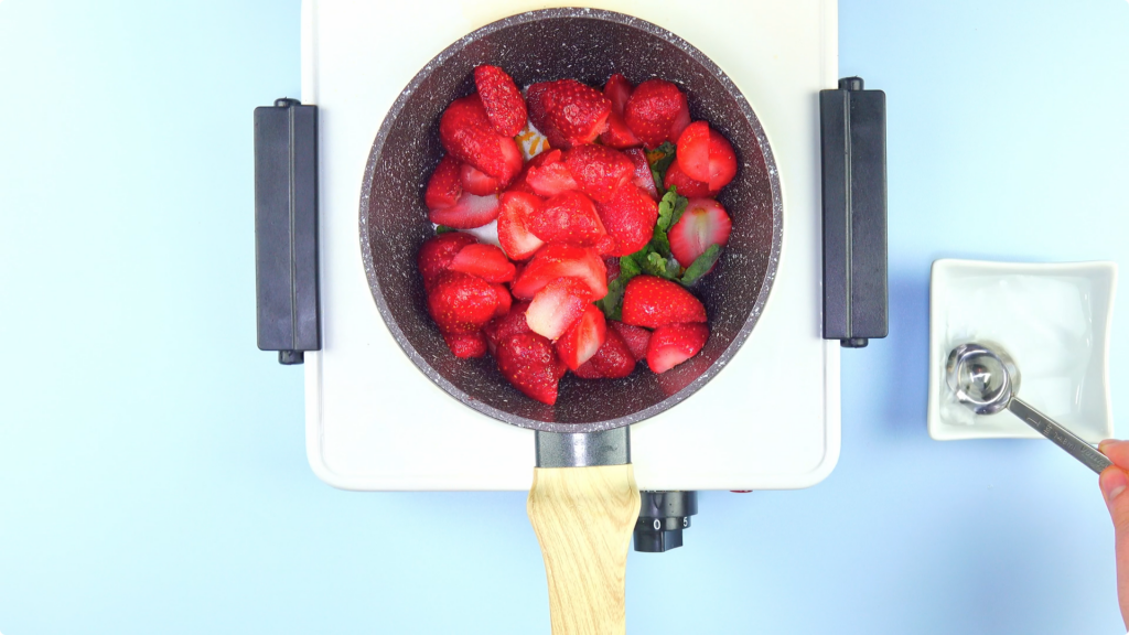 Strawberry quarters, mint, sugar, lemon in a pot over an electric hob