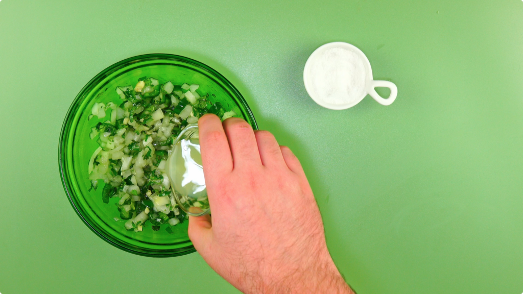 Adding lime juice from a small glass dish into a large glass bowl of onions, coriander and chillies