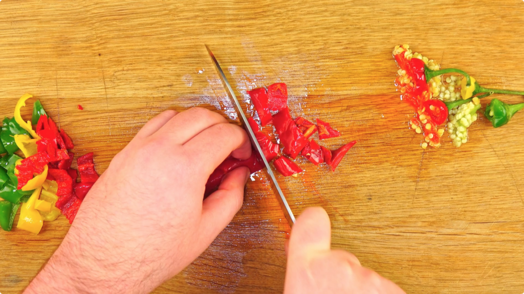 Chopping red, green and yellow chillies on a wooden chopping board