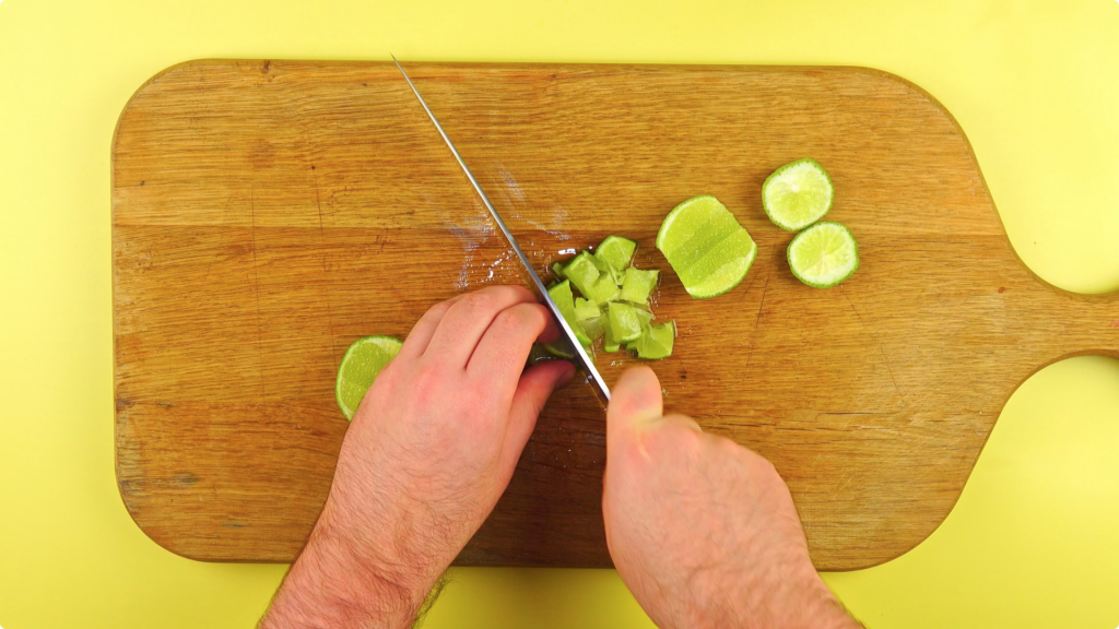 Photo from above of lime being diced finely with a knife on a wooden chopping board