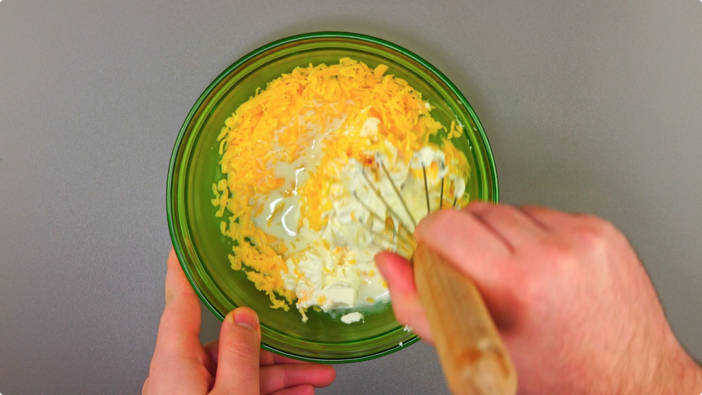 Whisking cheddar cheese, cream cheese and milk in a glass bowl