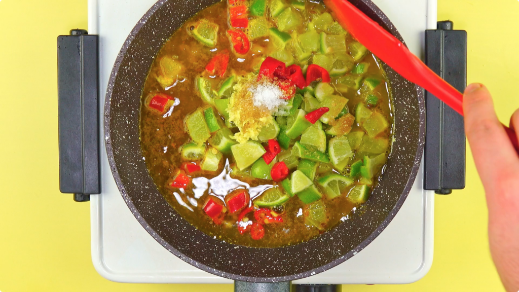 Lime, sugar, chilli, vinegar, salt, and spices in a skillet being stirred by a red spatula