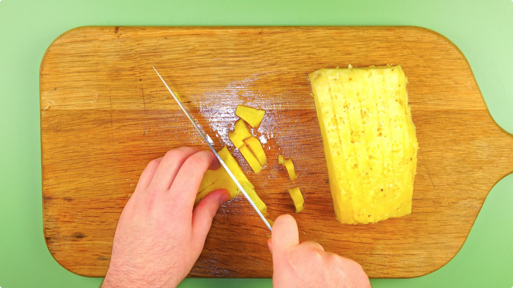 From above, a man chopping pineapple on a wooden chopping board
