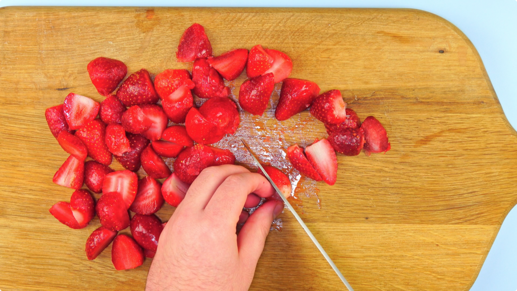 Hulling and quatering strawberries on a wooden chopping board
